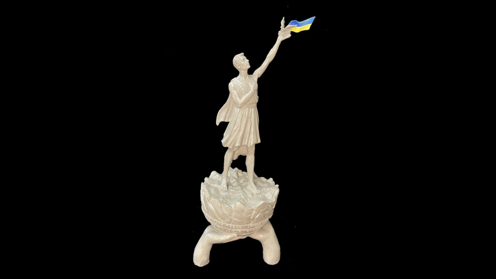a model of a statue holding aloft a dove a book and Ukrainian flag with the words Live Peace on the base