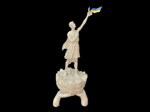 a model of a statue holding aloft a dove a book and Ukrainian flag with the words Live Peace on the base